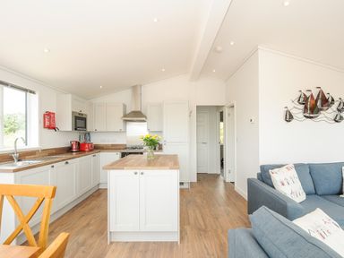 A kitchen with white cabinets and wooden countertops next to a blue sofa with pillows at Midway Lodge in Cawsand near Kingsand