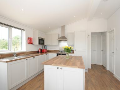 A kitchen with white cabinets wooden countertops a kitchen island with yellow flowers a window a microwave a toaster and a kettle at Midway Lodge in Cawsand near Kingsand