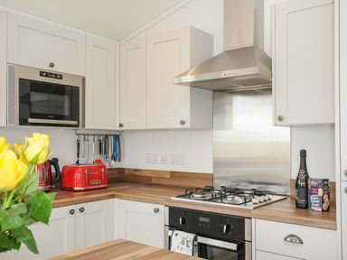 A kitchen with white cabinets a built-in microwave a red toaster and kettle a gas stove with hood and a bottle with snacks on the counter at Midway Lodge in Cawsand near Kingsand