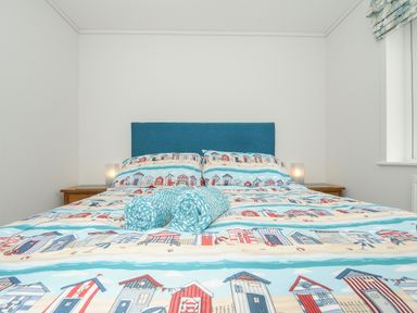 A bedroom with a bed with a blue headboard beach house print bedding and two rolled towels on the bed at Midway Lodge in Cawsand near Kingsand