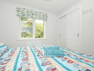 A bedroom with a bed covered in patterned bedding a window with a blind and a closed white closet door at Midway Lodge in Cawsand near Kingsand