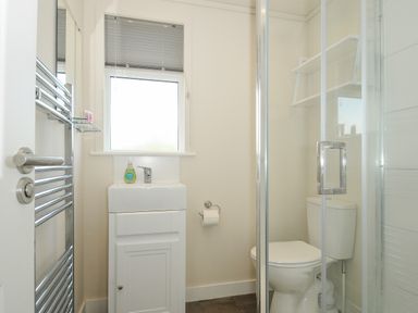 A small bathroom with a sink, toilet, shower enclosure, and window at Midway Lodge in Cawsand near Kingsand