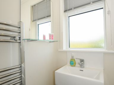 A bathroom sink with a soap dispenser under a frosted window and a glass shelf with toiletries at Midway Lodge in Cawsand near Kingsand