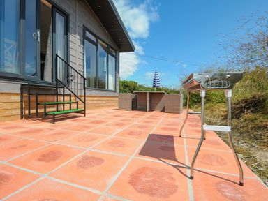 An outdoor patio with tiled floor a metal barbecue table seating area with chairs and an umbrella at Midway Lodge in Cawsand near Kingsand