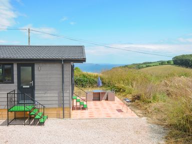 A small building with stairs and a patio area with table chairs umbrella and barbecue near the coast at Midway Lodge in Cawsand near Kingsand