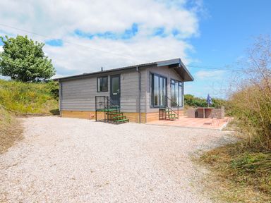 A small gray wooden house with stairs and a patio with outdoor furniture at Midway Lodge in Cawsand near Kingsand