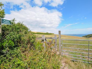 A countryside footpath gate next to a metal gate with a view of fields and the sea at Midway Lodge in Cawsand near Kingsand