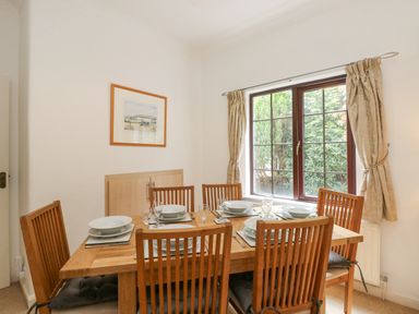 A dining room with a wooden table set for six next to a window with curtains at Brantfell Lodge in Bowness-On-Windermere