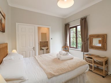 A bedroom with a bed with rolled towels on it a window with curtains a chair and a wicker-framed mirror at Brantfell Lodge in Bowness-On-Windermere