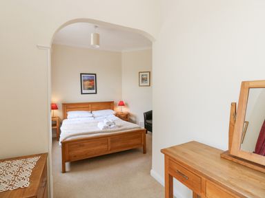 A bedroom with a wooden double bed with folded towels bedside tables with lamps and a wooden dresser with a mirror at Brantfell Lodge in Bowness-On-Windermere