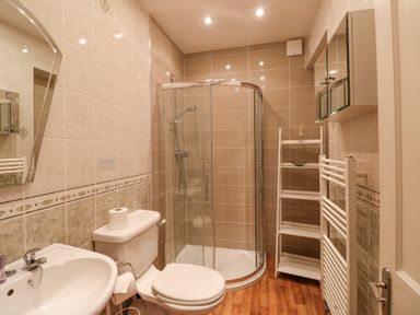 A bathroom with a toilet, sink, curved glass shower, shelving unit, towel radiator, and mirrored cabinet at Brantfell Lodge in Bowness-On-Windermere