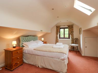 A bedroom with a double bed two bedside cabinets with lamps a window with floral curtains and a wooden chair at Brantfell Lodge in Bowness-On-Windermere