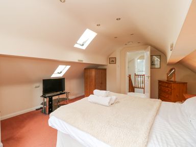 A bedroom with a bed, TV on a stand, wooden wardrobe, dresser, and skylights at Brantfell Lodge in Bowness-On-Windermere