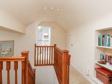 A hallway with wooden stair railing bookshelves on the wall and a door leading to a bathroom at Brantfell Lodge in Bowness-On-Windermere