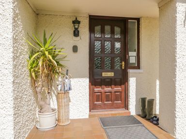 An entrance door with glass panels flanked by a potted plant an umbrella stand with umbrellas and a pair of boots at Brantfell Lodge in Bowness-On-Windermere
