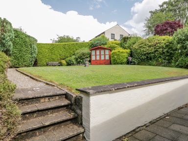 A garden with stone steps leading to a lawn with a red wooden shed and surrounded by hedges at Brantfell Lodge in Bowness-On-Windermere