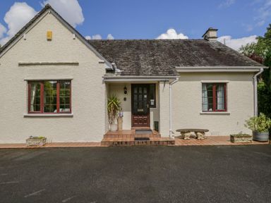 The front view of a single-story house with two windows a central door and plants on a tiled porch at Brantfell Lodge in Bowness-On-Windermere
