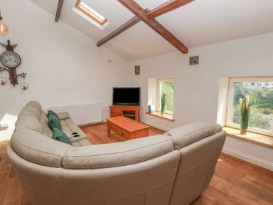 A living room with a curved sofa a wooden coffee table a television and windows with plants at Greenheart Cottage in Pontrhydyfen