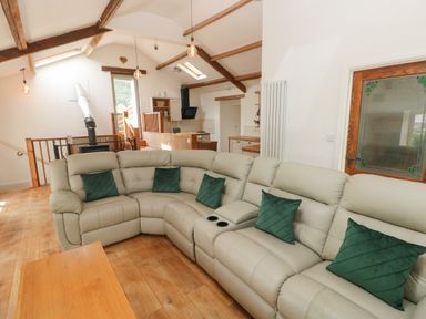 A living room with a curved beige sofa with green pillows wooden floor and ceiling beams at Greenheart Cottage in Pontrhydyfen