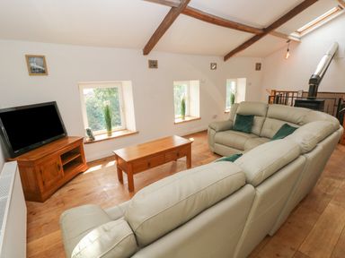 A living room with cream sofas a wooden coffee table a television on a wooden stand and windows on a slanted wall at Greenheart Cottage in Pontrhydyfen