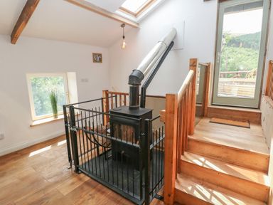 A wood stove with a metal guard in a room with wooden stairs and a door leading outside at Greenheart Cottage in Pontrhydyfen