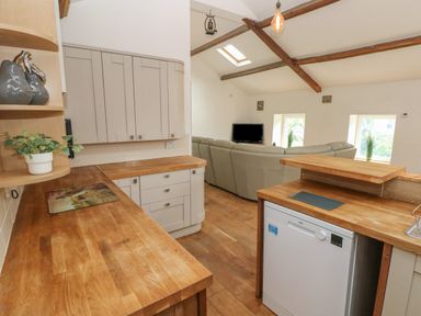 A kitchen area with wooden countertops and a dishwasher next to a living room with a sofa and a television at Greenheart Cottage in Pontrhydyfen