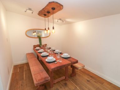 A dining room with a wooden table set with white dishes and benches on a wooden floor at Greenheart Cottage in Pontrhydyfen