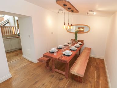 A dining area with a wooden table set with plates glasses and cutlery and wooden benches at Greenheart Cottage in Pontrhydyfen