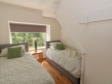 A bedroom with two single beds and a small wooden table near a window at Greenheart Cottage in Pontrhydyfen