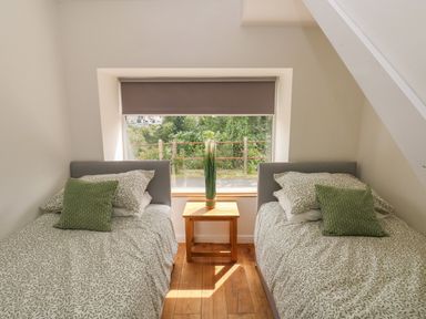 A bedroom with two single beds separated by a wooden bedside table with a plant on it at Greenheart Cottage in Pontrhydyfen