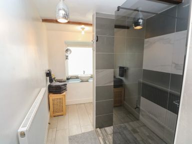 A bathroom with a walk-in shower, a wooden laundry basket with towels, a round basin sink on a windowsill, and a radiator at Greenheart Cottage in Pontrhydyfen