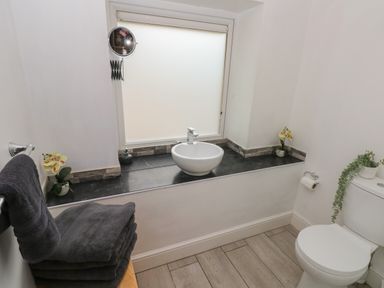 A bathroom with a round sink on a black countertop next to a toilet and folded towels at Greenheart Cottage in Pontrhydyfen