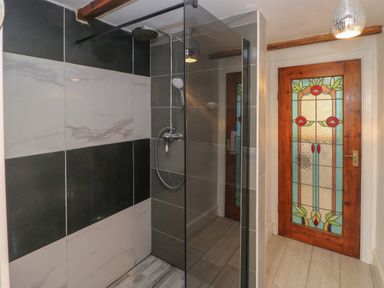 A bathroom with a walk in shower and a wooden door with stained glass at Greenheart Cottage in Pontrhydyfen