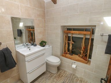 A bathroom with a white sink cabinet mirror toilet and wooden decorative items on a window at Greenheart Cottage in Pontrhydyfen