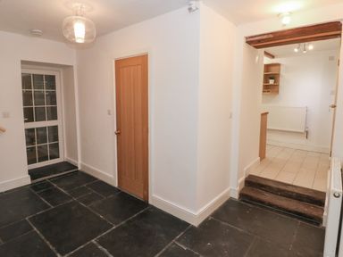 A hallway with a wooden door black tiled floor a glass door and stairs leading to a kitchen at Greenheart Cottage in Pontrhydyfen