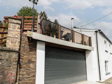 A closed garage door below a balcony with glass panels and wooden railings at Greenheart Cottage in Pontrhydyfen