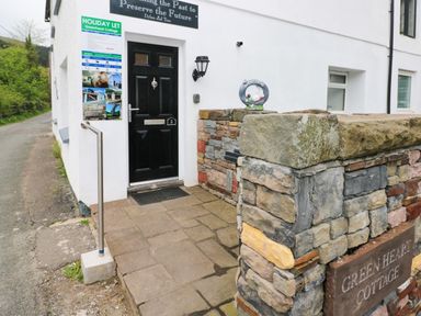 Front entrance with black door stone wall and holiday let sign at Greenheart Cottage in Pontrhydyfen