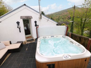 An outdoor patio area with a hot tub and outdoor seating next to a white building at Greenheart Cottage in Pontrhydyfen