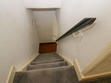 A narrow staircase with grey carpet and a black handrail on the right at 3 Nixon Terrace in Broughton Moor near Maryport