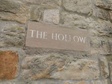 A stone wall with a plaque reading the hollow at The Hollow in West Woodburn