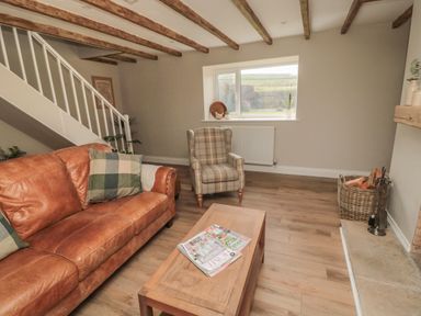 A living room with a leather sofa a plaid armchair a wooden coffee table magazines on the table a window stairs and a basket with firewood at The Hollow in West Woodburn