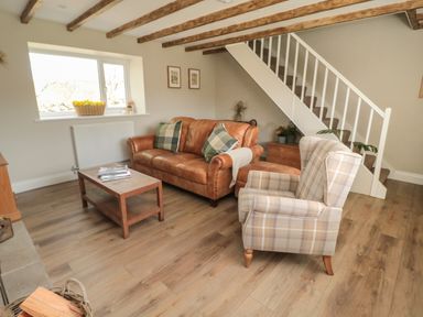 A living room with a brown leather sofa two green pillows a checkered armchair wooden coffee table and staircase at The Hollow in West Woodburn