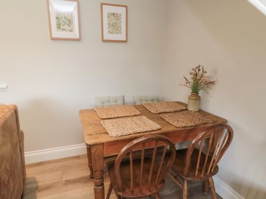 A wooden dining table with four woven placemats two wooden chairs and two framed botanical prints on the wall at The Hollow in West Woodburn