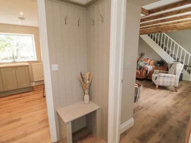 A hallway with wall hooks and a small bench with a vase of dried flowers next to a kitchen and a living room at The Hollow in West Woodburn