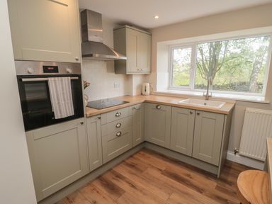 A kitchen with gray cabinets wooden countertops a stove oven kettle and a window showing trees at The Hollow in West Woodburn
