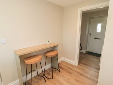 A small wooden bar table with two wooden stools in a hallway next to a white front door at The Hollow in West Woodburn