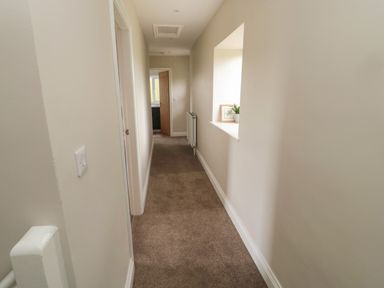 A hallway with a window ledge holding a plant and framed picture and an open door at the end of the corridor at The Hollow in West Woodburn