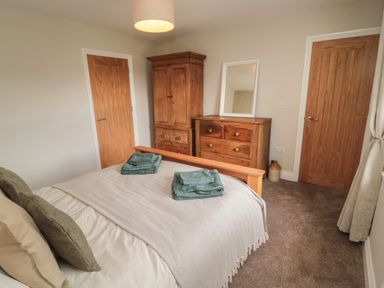A bedroom with a wooden bed a dresser a wardrobe two wooden doors and folded towels on the bed at The Hollow in West Woodburn