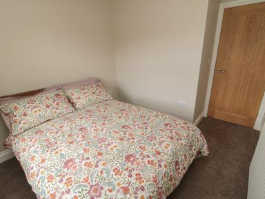 A bedroom with a bed covered in floral patterned bedding and a wooden door at The Hollow in West Woodburn