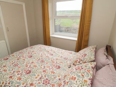 A bedroom with a bed with floral bedding next to a window with mustard curtains at The Hollow in West Woodburn